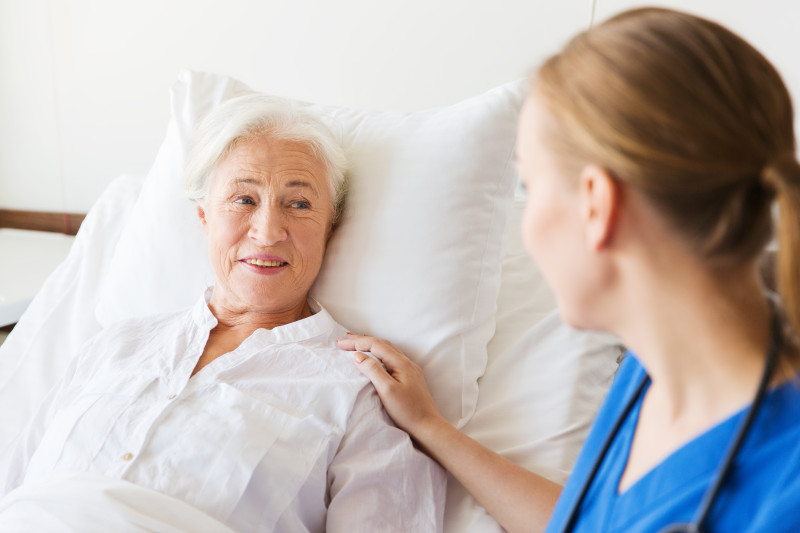Nurse sitting next to a patient in a hospital bed with her had on their shoulder. 